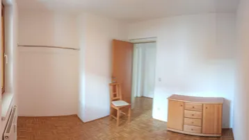 Helles Schlafzimmer mit Parkettboden, Fenster und einem Kleiderständer, bereit zur individuellen Einrichtung.