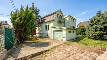 Grünes Einfamilienhaus mit Mansarddach, Garage und Gartenbereich unter blauem Himmel.