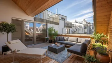 Geräumige Dachterrasse mit bequemen Loungemöbeln, Sonnenliege und Holzboden für entspannte Stunden im Freien.