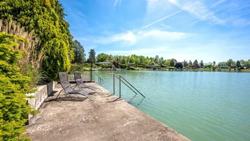 Betonsteg mit Liegestühlen und direktem Zugang zum See unter strahlend blauem Himmel.