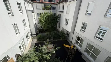 Grüner Innenhof mit Spielplatz und Rutsche, umgeben von den Fassaden der Wohngebäude.