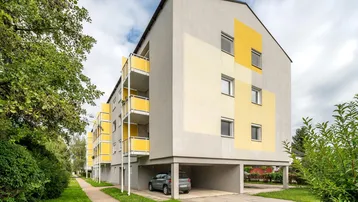 Modernes Mehrfamilienhaus mit gelben Akzenten und Carport-Parkplätzen im Freien.