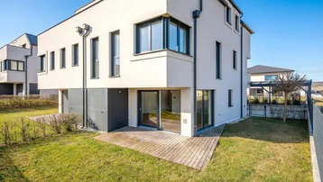 Moderne Hausfassade mit großem Garten und Holzterrasse.