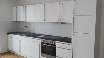 Moderne Einbauküche mit weißen Schränken, dunkler Arbeitsplatte und hellem Holzboden.