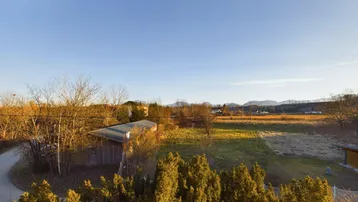 Weitläufiger Blick über Felder und Bäume bis zu den fernen Bergen unter klarem Himmel.