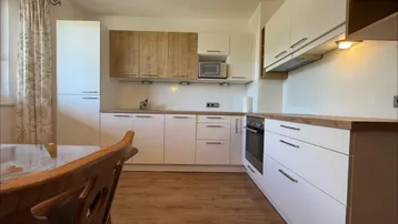 Moderne Küche mit weißen und holzfarbenen Schränken, ausgestattet mit Einbaugeräten und Holzboden.