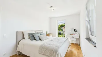 Helles Schlafzimmer mit Holzboden, großem Bett und Zugang zu einem kleinen Balkon.