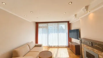 Helles Wohnzimmer mit Parkettboden, beigem Sofa, Kamin und Zugang zum Balkon.