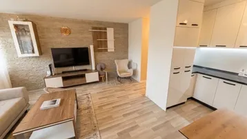 Moderner offener Wohnbereich mit heller Holzoptikboden und integrierter Küche, ideal für geselliges Beisammensein.