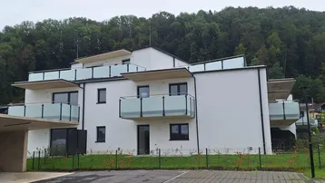 Modernes Mehrfamilienhaus mit Balkonen, Carport und Blick ins Grüne.