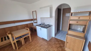 Heller Wohnbereich mit kleiner Küchenzeile, Essplatz und Holzparkettboden in einem älteren Gebäude.