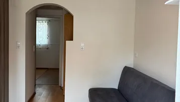 Gemütliches Wohnzimmer mit Holzboden und einem Durchgang zu einem weiteren Raum.