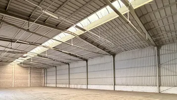 Geräumige, leere Lagerhalle mit hoher Decke, Oberlichtern und Betonboden, ideal für industrielle Nutzung.