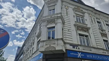Historisches Eckgebäude mit klassischer Fassadenarchitektur und großen Fenstern unter bewölktem Himmel.