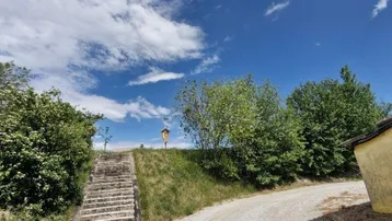 Schotterweg und Steintreppe führen einen grasbewachsenen Hügel hinauf unter blauem Himmel.