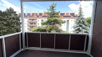 Überdachter Balkon mit Blick auf umliegende Gebäude und grüne Bäume, ideal zum Entspannen im Freien.