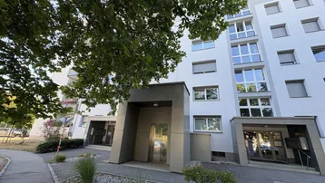 Eingangsbereich eines modernen Mehrfamilienhauses mit gepflegter Außenanlage und Bäumen.