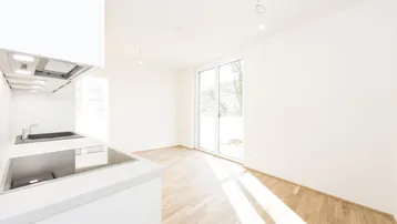 Helle, moderne Küche mit weißen Schränken, Induktionskochfeld und Zugang zu einem sonnigen Außenbereich.