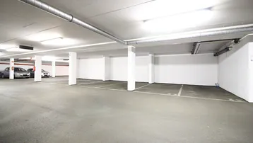 Geräumige und helle Tiefgarage mit markierten Stellplätzen und sichtbaren Versorgungsleitungen an der Decke.