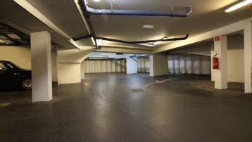 Geräumige Tiefgarage mit robustem Betonboden, sichtbaren Versorgungsleitungen und stabilen Säulen.