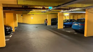 Tiefgarage mit mehreren Stellplätzen, gelben Wänden und sichtbaren Installationen an der Decke.