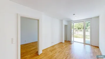 Helles, leeres Wohnzimmer mit Holzboden und Zugang zu einer Terrasse oder einem Gartenbereich.