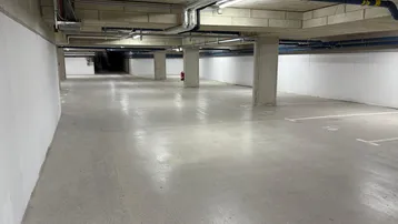 Geräumige Tiefgarage mit Betonboden, sichtbaren Leitungen und markierten Parkplätzen.