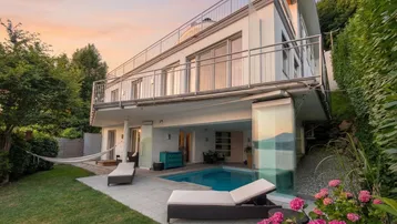 Moderne Villa mit privatem Pool, Liegewiese und Blick auf den See bei Sonnenuntergang.