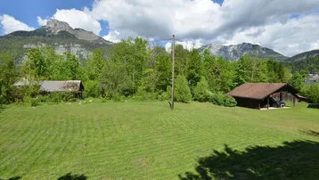 Weitläufige Grünfläche mit Bergblick und ländlicher Umgebung unter blauem Himmel.