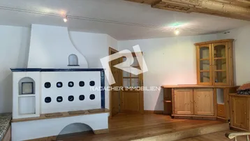 Gemütliches Wohnzimmer im alpinen Stil mit traditionellem Kachelofen und Holzbalkendecke.