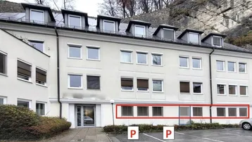 Mehrstöckiges Gebäude mit zahlreichen Fenstern und Dachgauben, gelegen an einem Berghang mit Parkplätzen.