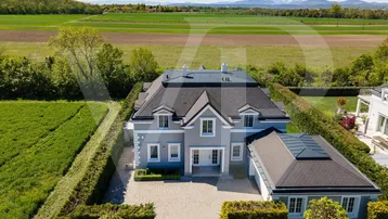 Luftaufnahme einer eleganten Villa mit gepflegtem Garten und weitem Blick auf die Landschaft und Berge.