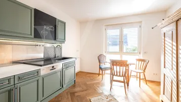 Moderne Wohnküche mit grünen Schränken, Holzboden und Essbereich am Fenster.