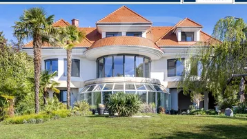 Großzügige Villa mit gepflegtem Vorgarten, Palmen und einem gläsernen Wintergarten.