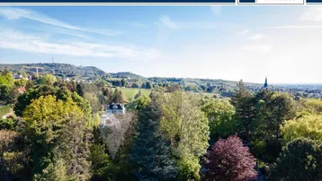 Weitläufiger Blick über eine grüne Hügellandschaft mit vereinzelten Häusern und einem Kirchturm.