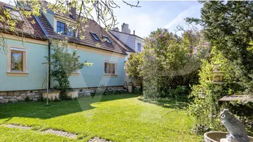 Gepflegter Gartenbereich hinter dem Haus mit Rasenfläche und dekorativen Elementen unter blauem Himmel.