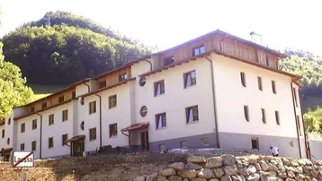 Mehrstöckiges Gebäude mit heller Fassade und Holzelementen in einer grünen Berglandschaft.