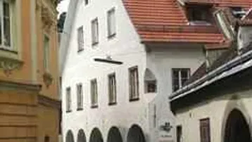Historisches Gebäude mit Arkaden und rotem Ziegeldach in einer engen Gasse.