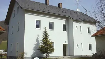 Weißes Wohnhaus mit Satteldach und grüner Umgebung, eingebettet in eine hügelige Landschaft.
