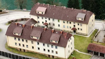 Zwei Mehrfamilienhäuser mit Satteldächern, umgeben von Grünflächen und einer Straße.