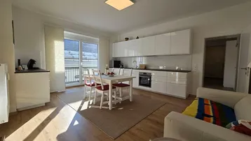 Helles, offenes Wohn-Esszimmer mit integrierter Küche, Holzboden und Zugang zum Balkon.