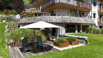 Geräumige Terrasse mit Holzdeck, Gartenmöbeln und Blick auf die Berge und das Gebäude.