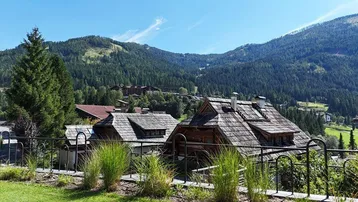 Blick auf traditionelle Holzhäuser mit Schindeldächern vor einer malerischen Berglandschaft unter blauem Himmel.