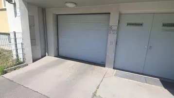 Einfahrt zu einer Tiefgarage mit Rampe und geschlossenem Garagentor in einem modernen Gebäude.