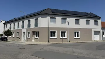 Modernes Mehrfamilienhaus mit Photovoltaikanlage und zweifarbiger Fassade an einer Straßenecke.