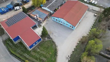 Luftaufnahme des Gewerbegebiets mit mehreren Gebäuden, darunter eines mit Solaranlage auf dem Dach und weiten Freiflächen.