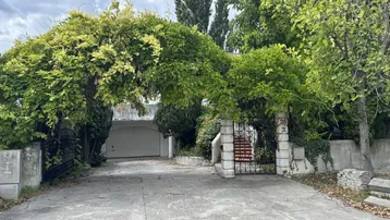 Zufahrt zu einem Anwesen mit Garage, umgeben von üppiger Vegetation und einem bewachsenen Torbogen.