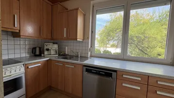 Funktionale Küche mit Holzschränken, weißen Fliesen und Blick ins Grüne durch das Fenster.
