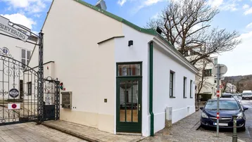 Weißes Gebäude mit grünen Akzenten und Eingangstür an einer gepflasterten Straße.