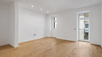 Helles, leeres Zimmer mit neuem Holzboden und Zugang zu einem französischen Balkon.